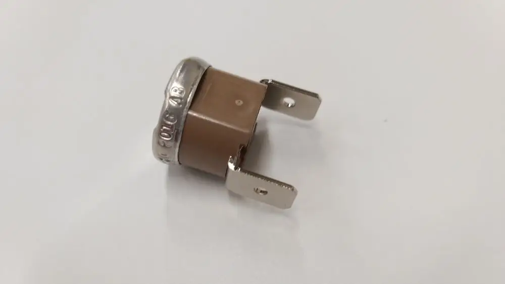 Brauner Temperaturbegrenzer mit metallischem Rand und zwei Anschlüssen, im Hintergrund weiß. Produkt von Remeha.